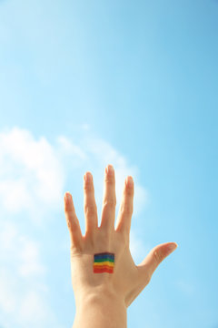 Female hand with painted rainbow flag and blue sky on background. Sexual minority concept
