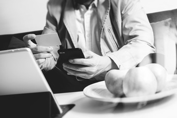 hipster hand using smart phone,digital tablet docking keyboard,holding cradit card payments online business,sitting on sofa in living room,work at home concept,black and white