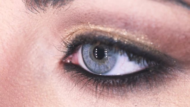 Woman's eye with gold eye shadow opens- macro