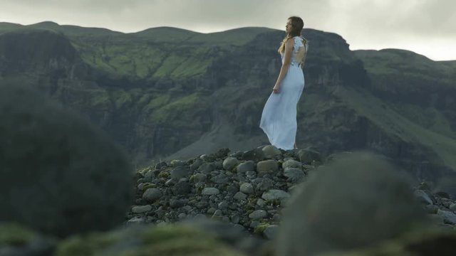 Woman in dress, stands on windy mountain peak