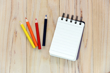 Blank note book paper (notepad) for writing information with color pencil on wooden table. view from above