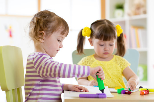 Two beautiful children girls are drawing in kindergarten or preschool.