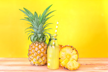 The Bottles of pineapple juice with sliced pineapple fruit on wooden table with vibrant yellow background , summer fruit drink concept