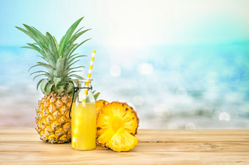 The Bottles of pineapple juice with sliced pineapple fruit on wooden table with abstract  blue sea background , summer fruit drink concept