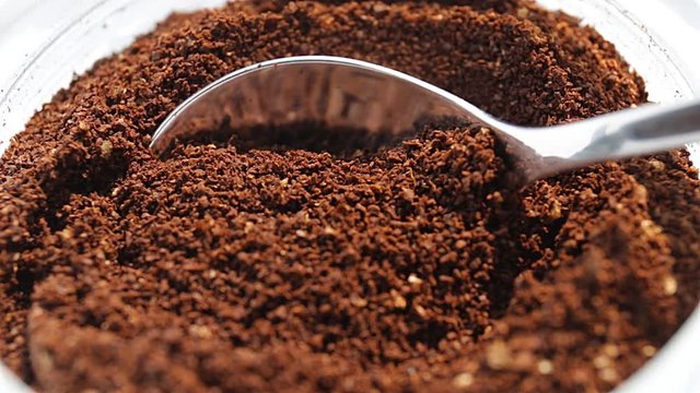 Coffee dosage from a jar with a small spoon on bright white background, macro and close up 