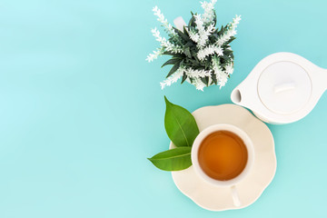 Top view shot of a hot cup of tea with green leaf and flower on blue background , Organic Tea ceremony time concept