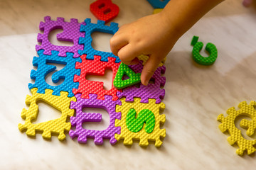 Colorful foam puzzle letters and numbers in kid's hands on a light table
