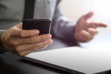 close up of businessman working with mobile phone and laptop computer on wooden desk in modern office