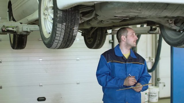 Car mechanic is checking car suspension on crossover in car repair service
