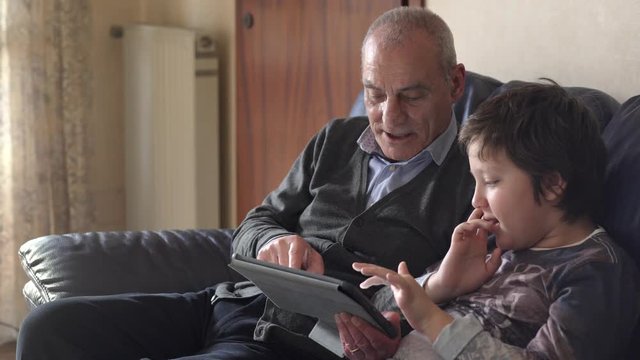 Portrait of Grandfather and grandson on the couch laugh and jokes using tablet