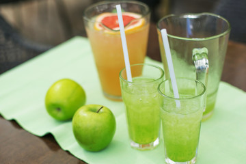 green and orange lemonade with ice and apples. Orange and lemon lemonade in pitchers and glasses