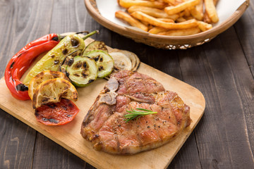 Grilled pork, vegetables and potato chips on wooden floor