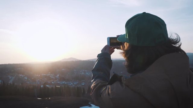 Young tourist man taking picture of sunset. Send photos from his trip to the social network.