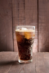 Cola in glass with ice on wooden background