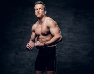 Portrait of shirtless athletic male with crossed arms over dark grey background.