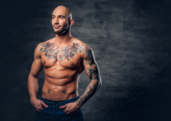 Fototapeta na wymiar Shaved head, muscular male with tattoos on his torso over grey vignette background.