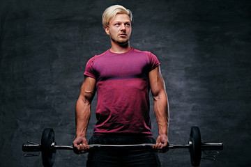 Fototapeta na wymiar A blond, athletic male dressed in a red sportswear holds barbel.