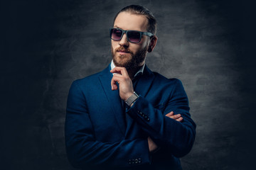 A stylish bearded male dressed in a suit and sunglasses over dark grey background.