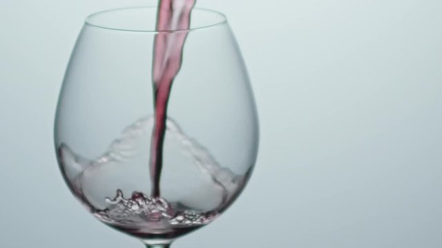 Slow motion shot with close up of red wine flowing into wineglass isolated on grey background