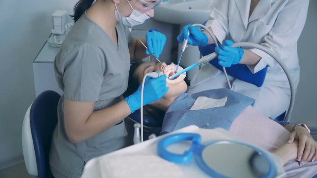 Young woman sitting in dental chair. Doctor with dental nurse treating a patient, scaling and polishing the teeth.