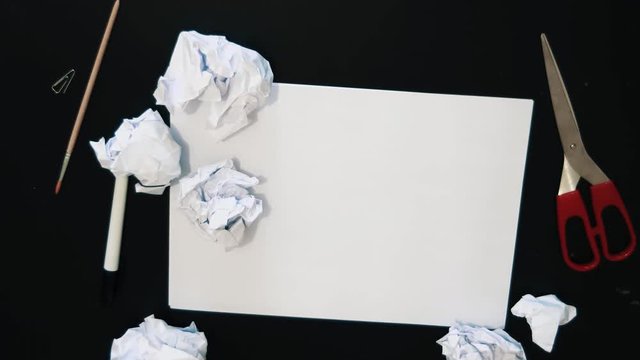 Crumpled paper pieces falls on black table with white sheet red scissors and bunch of brushes