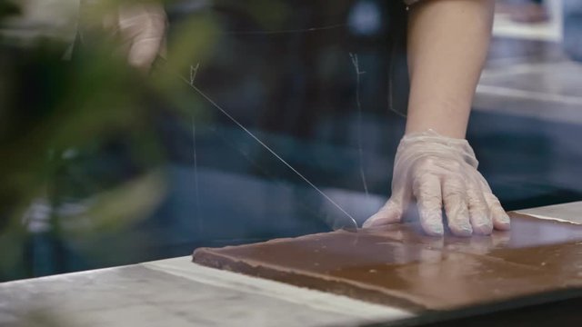 Tracking closeup of female confectioner cutting fudge with knife on paper