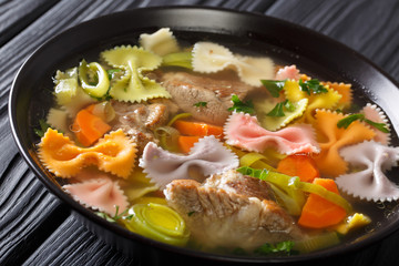 Italian soup with pork, colored farfalle pasta and vegetables close-up. horizontal