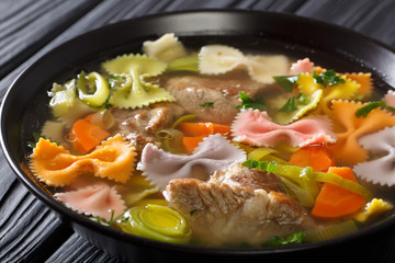 Delicious soup with meat, multi-colored farfalle pasta and vegetables close-up. horizontal