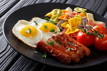 Fried eggs with sausages, colored farfalle pasta and tomatoes closeup. horizontal