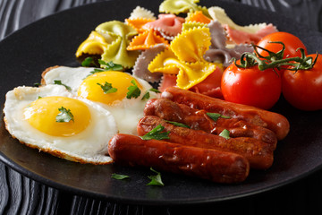 Homemade breakfast: fried eggs, sausages, colored farfalle pasta and tomato close-up. horizontal
