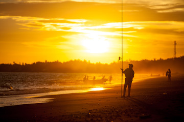 Fototapeta premium Silhouette of a girl on the beach with a fishing rod in the summer