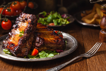Roasted ribs, served on an old plate. Dark or black background.