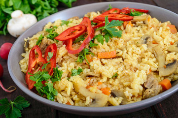 A traditional Asian dish - pilaf with meat, mushrooms and pepper capi in a bowl on a dark wooden background.