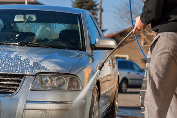 Fototapeta premium Worker in auto service is washing a luxury car by water hoses, backlight