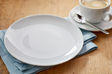 Empty white plate on blue napkin and coffee