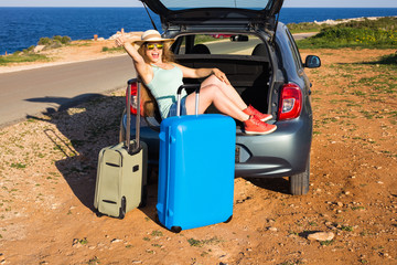 Travel, summer holidays and vacation concept - Young woman with suitcases on car trip. She is sitting in car back and gesture thumbs up.