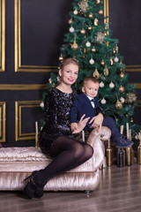 Portrait of happy mother and adorable baby celebrate Christmas. New Year's holidays. Toddler with mom in the festively decorated room with Christmas tree and decorations.