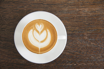 Coffee cup latte art with hearth shape foam top view on wooden table background in coffee shop