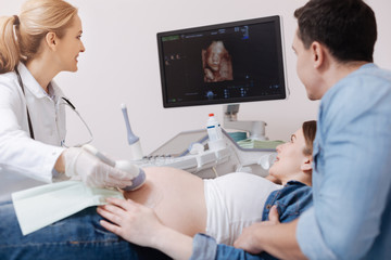 Cheerful medic providing ultrasound scanning of pregnant belly at work