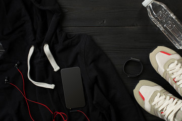 Athlete's set with female clothing, sneakers and bottle of water on dark background