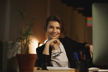 Happy young woman designer sitting in office at night