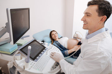 Joyful obstetrician providing pregnant abdomen checkup at work