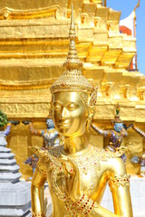 Fototapeta premium Golden Kinnaree holding flower against pagoda background on display at wat pra kaew in Bangkok, Thailand.