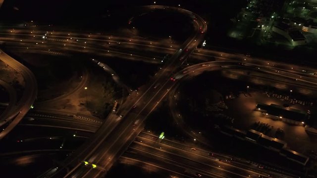 AERIAL HELI SHOT: Flying above lit up with lights gigantic multi level interchange road junction on highway with on-ramps and off-ramps. Dense traffic in commercial zone, vehicles traveling at night