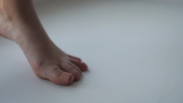 Woman bare feet standing on toes on white floor turning on point, bandage around toes thumb
