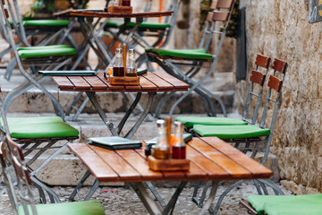 Wooden chairs and tables with a menu, salt and oil in a European street cafe or restaurant.