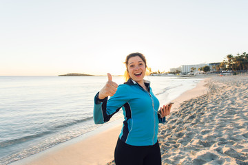 Outdoor sport, fitness gadget and people concept - Smiling female fitness show thumbs up and holding smartphone with earphones.