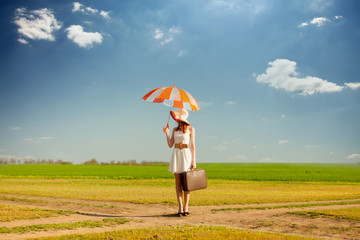 photo of beautiful young woman with suitcase and umbrella on the road near field background