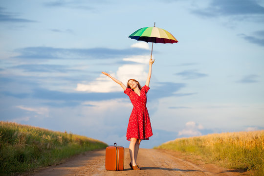 photo of beautiful young woman with suitcase and umbrella on the road near field background