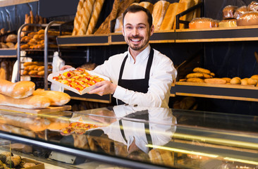 Male shop assistant demonstrating fresh delicious pastry in bakery